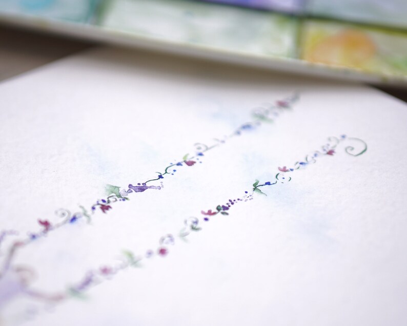 Pode incluir: Um cart&atilde;o branco com um delicado desenho floral em tons de azul, roxo e rosa. O desenho apresenta uma s&eacute;rie de pequenas flores e folhas dispostas em um padr&atilde;o fluido.