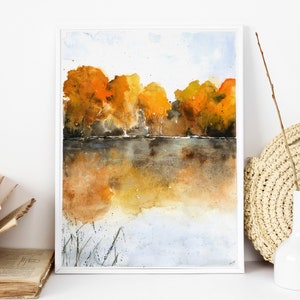 Puede incluir: Pintura acuarela de una escena de lago con una hilera de &aacute;rboles en colores oto&ntilde;ales, incluyendo amarillo, naranja y rojo. Los &aacute;rboles se reflejan en el agua, que es de un color marr&oacute;n apagado. El cielo es de un azul claro con algunas nubes.