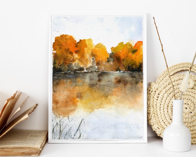 Puede incluir: Pintura acuarela de una escena de lago con una hilera de &aacute;rboles en colores oto&ntilde;ales, incluyendo amarillo, naranja y rojo. Los &aacute;rboles se reflejan en el agua, que es de un color marr&oacute;n apagado. El cielo es de un azul claro con algunas nubes.