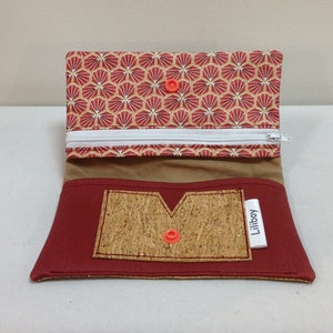 May include: Open red and gold patterned wallet with a cork pocket and a white zipper. The interior features a tan lining and a red button closure. The label reads "Liliboy".