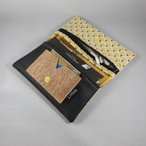 May include: A black and yellow zippered wallet with a cork card holder. The wallet has a yellow fan-shaped pattern on the top flap and a black leather-like material on the bottom. The cork card holder has a yellow snap closure and the word "Liliboy" printed on it.