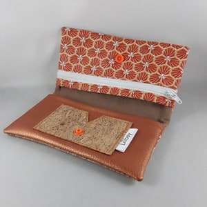 May include: Open, copper-colored wallet with a geometric patterned flap and a cork accent. The wallet features a white zipper, orange snap closures, and a small white tag that reads "Liliboy".