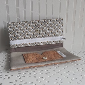 May include: Open wallet with a fan pattern in gray, white, and gold. The wallet has a white zipper and a cork accent with a button closure. The interior is a light gray color.