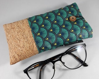 May include: Eyeglass case with a cork and patterned fabric design, next to a pair of black-rimmed spectacles. The case features a button closure and a teal, navy, and yellow fan-shaped pattern. The spectacles have a black frame.