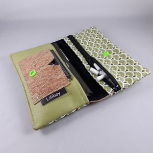 May include: A green and patterned wallet with a cork pocket and a black zipper. The wallet has a green interior and a black zipper. The wallet has the text "Liliboy" on a black tag.