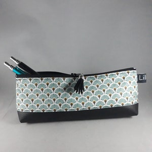May include: A rectangular pencil case with a black zipper and tassel. The case features a pattern of teal and gold fan shapes on a white background, with a black faux leather base. Two pens are visible inside.