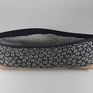 May include: A navy blue pencil case with a floral pattern and a cork base. The case has a black zipper and a small tassel. The interior lining is a light floral pattern. The zipper pull has the word "lil" printed on it.