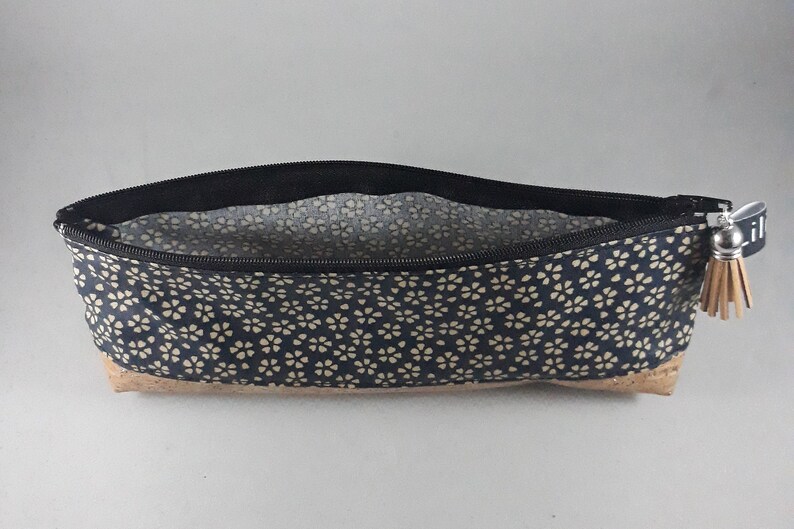 May include: A navy blue pencil case with a floral pattern and a cork base. The case has a black zipper and a small tassel. The interior lining is a light floral pattern. The zipper pull has the word "lil" printed on it.