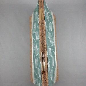 May include: A rectangular clutch with a light green and white leaf pattern. The clutch has a cork exterior with a gold-colored clasp. The design features a botanical theme, suitable for carrying essentials.