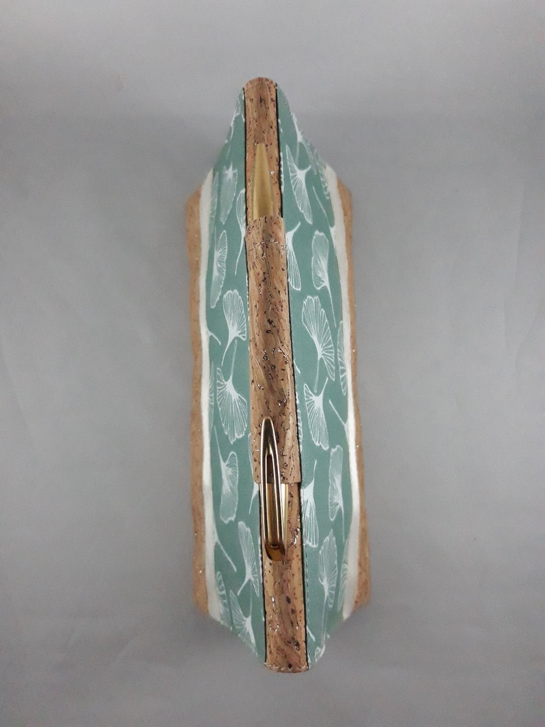 May include: A rectangular clutch with a light green and white leaf pattern. The clutch has a cork exterior with a gold-colored clasp. The design features a botanical theme, suitable for carrying essentials.