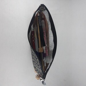 May include: A navy blue pencil case with a black zipper, filled with pens and pencils. The case has a pattern of small white and yellow dots. The interior lining is a light gray with a white floral pattern.