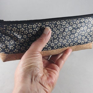 May include: A rectangular pencil case with a navy blue floral pattern and a cork base. The case has a black zipper and a small tassel. The word "Lil" is printed on a small black tag.