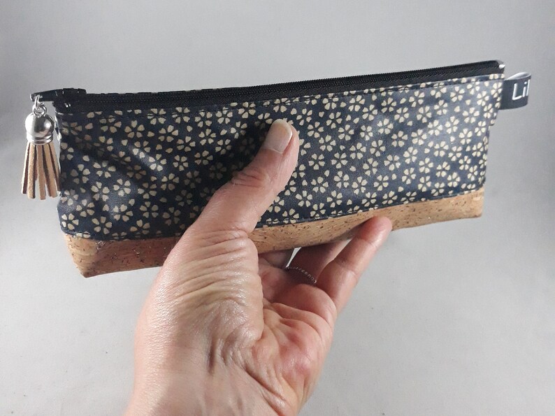 May include: A rectangular pencil case with a navy blue floral pattern and a cork base. The case has a black zipper and a small tassel. The word "Lil" is printed on a small black tag.