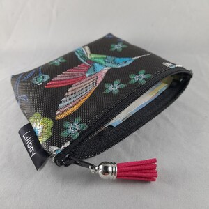 Op de afbeelding: Zwarte etui met ritssluiting en een kleurrijk borduurontwerp van een kolibrie. De etui heeft een roze kwast en een klein label met "Liliboy". De kolibrie is afgebeeld met blauwe, roze en groene veren.