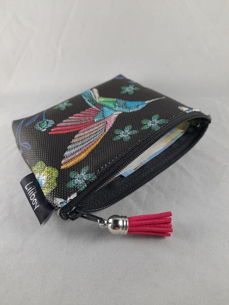 Op de afbeelding: Zwarte etui met ritssluiting en een kleurrijk borduurontwerp van een kolibrie. De etui heeft een roze kwast en een klein label met "Liliboy". De kolibrie is afgebeeld met blauwe, roze en groene veren.