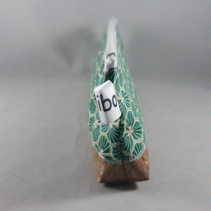 May include: A green and gold patterned pencil case with a cork base and a white zipper. The pencil case has a tag that reads "ibo". The case is designed to hold pens, pencils, and other stationery items.