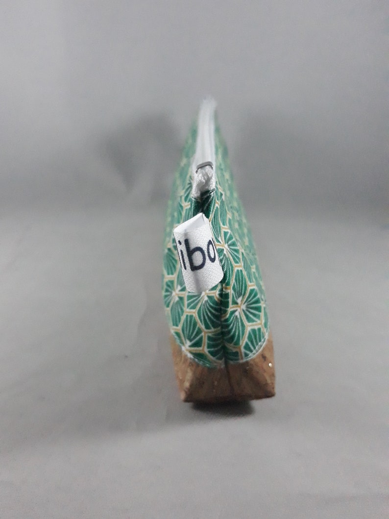 May include: A green and gold patterned pencil case with a cork base and a white zipper. The pencil case has a tag that reads "ibo". The case is designed to hold pens, pencils, and other stationery items.