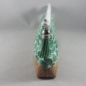 May include: A green and gold geometric pattern cosmetic bag with a cork base. The bag has a white zipper and a silver zipper pull. The bag is designed to hold makeup and other beauty products.