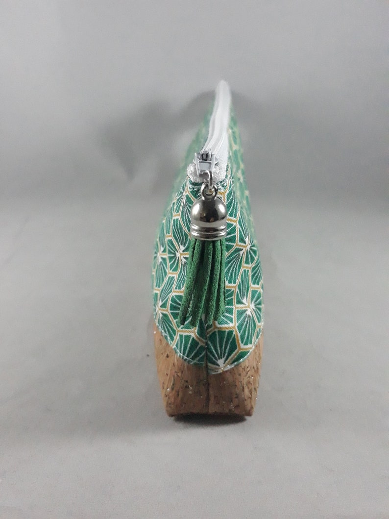 May include: A green and gold geometric pattern cosmetic bag with a cork base. The bag has a white zipper and a silver zipper pull. The bag is designed to hold makeup and other beauty products.