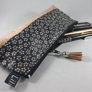 May include: A rectangular pencil case with a black zipper and a tassel. The top section is made of cork, while the main body features a navy blue floral pattern. The case is partially open, revealing pens and a pencil.