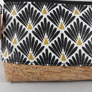 May include: A rectangular pouch with a black zip and a brown tassel. The pouch features a white fabric with a repeating black and gold fan-like pattern. The base is made of cork material.