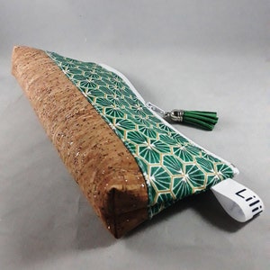 May include: A rectangular pencil case with a cork and geometric patterned design. The case features a brown cork body with a green and gold geometric pattern on the top. A white zipper and green tassel complete the design. The tag reads "Lili".