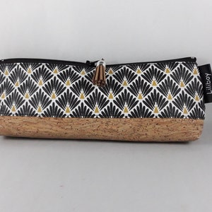May include: A rectangular pencil case with a black zip and a cork base. The upper section has a repeating black and gold fan pattern on a white background. A small tassel and a tag reading "Liliboy" are attached.