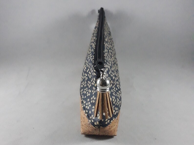 May include: A navy blue and beige floral print cosmetic bag with a cork base. The bag has a black zipper and a silver tassel. The bag is designed to hold makeup and other beauty products.