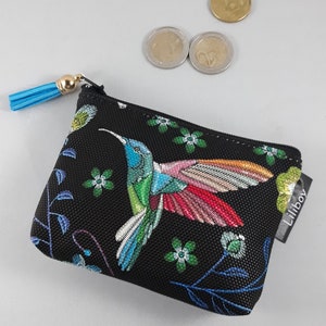 Op de afbeelding: Zwarte portemonnee met een kleurrijk geborduurde kolibrie. De kolibrie heeft blauwe, groene en rode details. De portemonnee heeft een blauwe kwast en het merklabel "Liliboy".