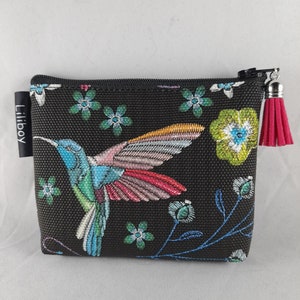 Op de afbeelding: Zwarte etui met ritssluiting met een kleurrijk geborduurd kolibrie- en bloemenontwerp. De kolibrie heeft blauwe, groene en roze veren. De etui heeft een roze kwast en de merknaam "Liilboy" op een klein label.