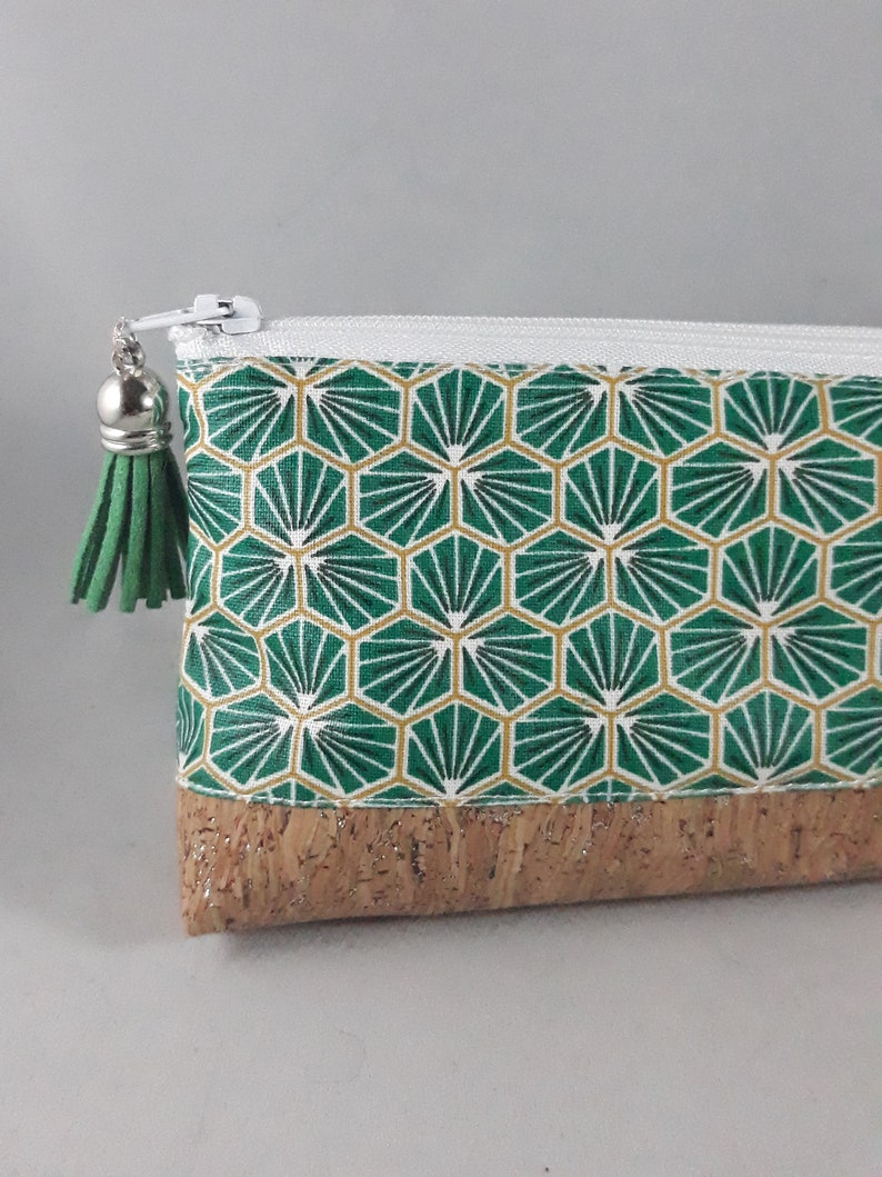 May include: A small, rectangular pouch with a white zipper and a green tassel. The pouch features a geometric pattern in green and gold, with a cork base. The zipper pull is silver.