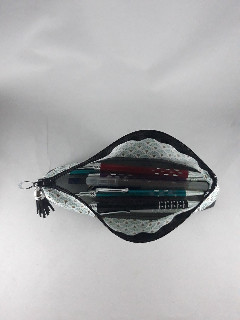 May include: Open pencil case with a black zipper and tassel. The interior features a light blue and white fan pattern, holding various pens and pencils. The case is open, displaying the contents against a white background.
