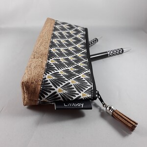 May include: A rectangular pencil case with a cork base and a black and white floral pattern. The case has a black zip and a brown tassel. Two pens are partially visible. The label reads "Liliboy".