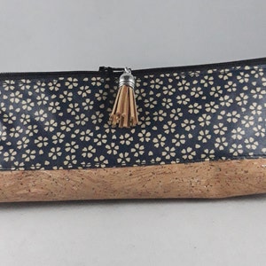 May include: A rectangular pencil case with a navy blue floral pattern on the top half and a cork bottom. The case has a black zipper, a small tassel, and a tag that reads "Lil".