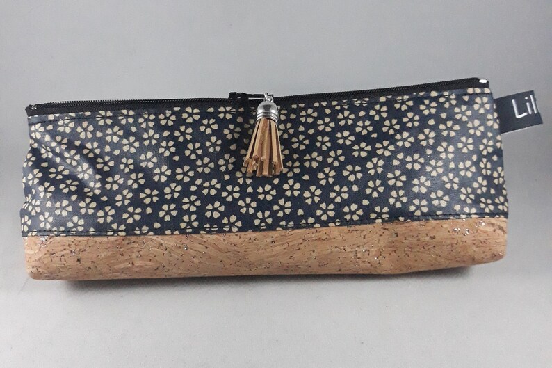 May include: A rectangular pencil case with a navy blue floral pattern on the top half and a cork bottom. The case has a black zipper, a small tassel, and a tag that reads "Lil".