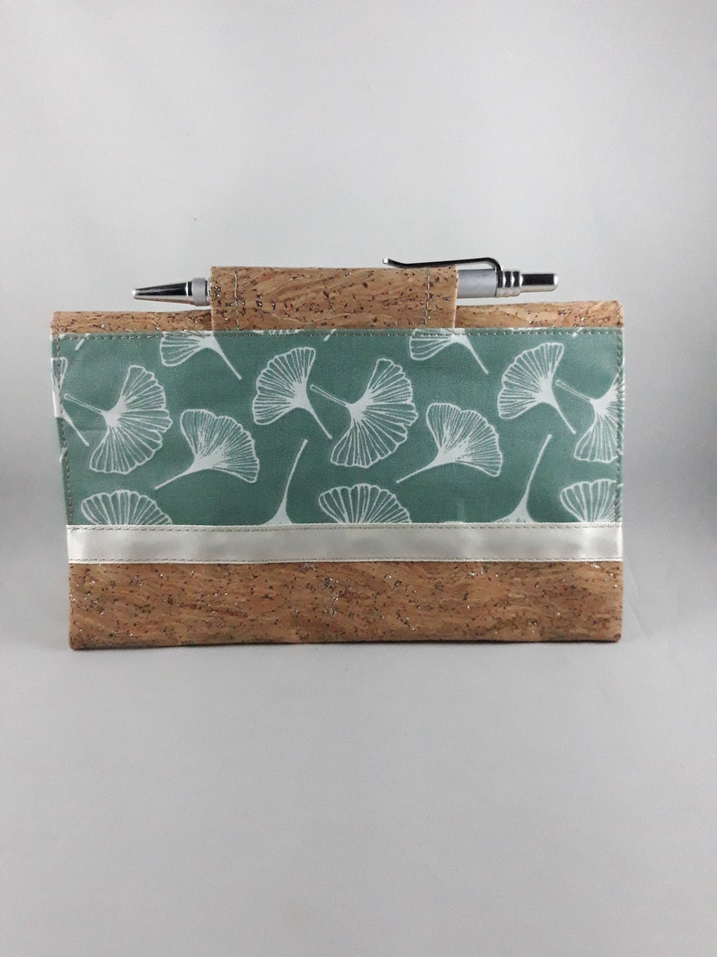 May include: A rectangular cork notebook cover with a pen holder. The cover features a teal fabric panel with white ginkgo leaf patterns and a silver ribbon accent. A silver pen rests in the holder, ready for use.