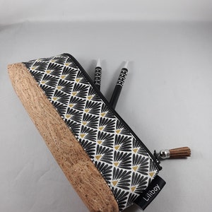 May include: A pencil case with a black and white floral pattern and a cork base. The pencil case has a black zip and a brown tassel. Two black and white pens are inside the case. The label says "Liliboy".