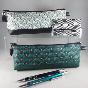 May include: Two pencil cases with a fan-shaped pattern in teal, gold, and white, with black trim and zippers. One case has a black tassel. The image also shows two pens and a business card holder with the text "LILIBOY cr&eacute;ations".