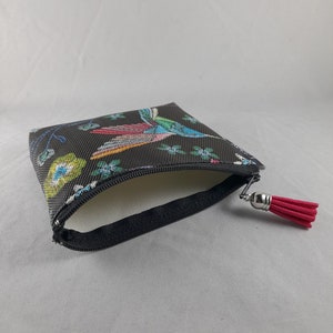 Op de afbeelding: Een kleine, zwarte etui met ritssluiting en een kleurrijk vogel- en bloemenpatroon. De etui heeft een rode kwast aan de ritstrekker. De binnenkant is wit.
