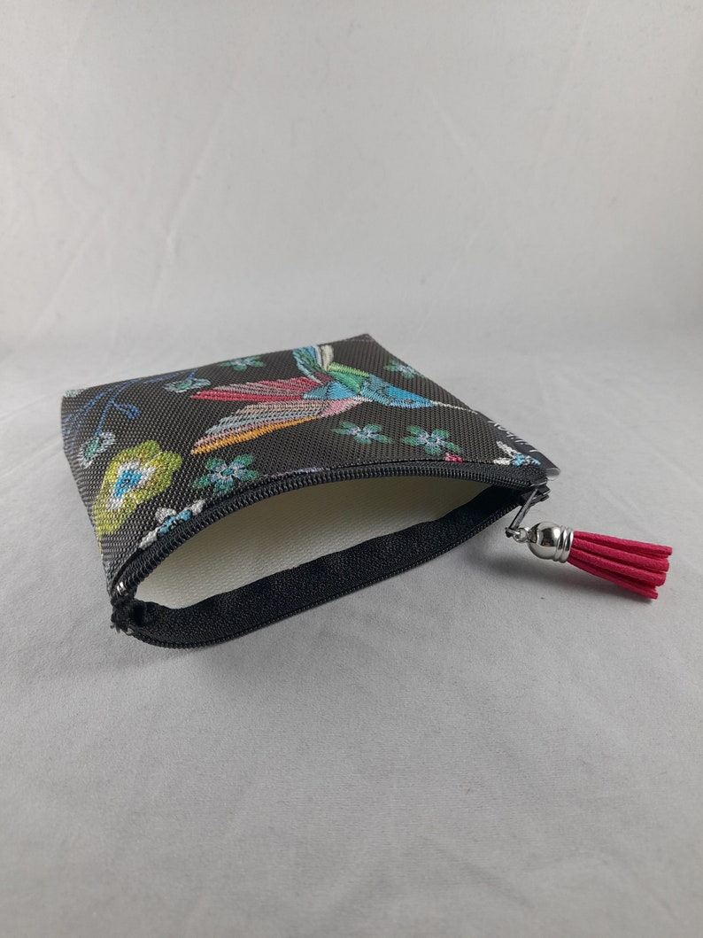 Op de afbeelding: Een kleine, zwarte etui met ritssluiting en een kleurrijk vogel- en bloemenpatroon. De etui heeft een rode kwast aan de ritstrekker. De binnenkant is wit.