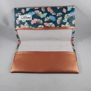 May include: Open eyeglass case with a teal, pink, and blue floral pattern. The case has a copper-colored trim and a copper-colored leather bottom. The interior is white mesh. The text "Liliboy" is visible on the top flap.