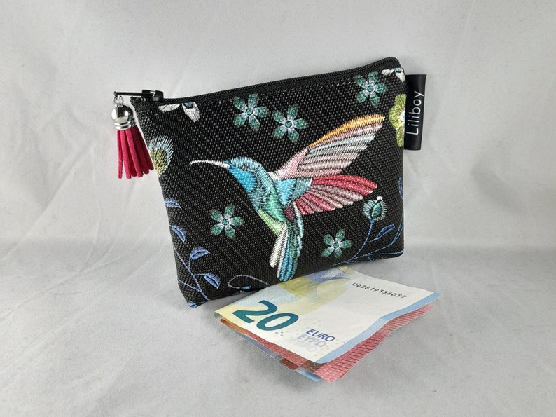 Op de afbeelding: Zwarte etui met ritssluiting en een kleurrijk kolibrie-ontwerp. De kolibrie is afgebeeld met blauwe, roze en rode veren, omringd door bloemmotieven. Een roze kwastje hangt aan de ritstrekker. De merknaam "Liliboy" is zichtbaar.