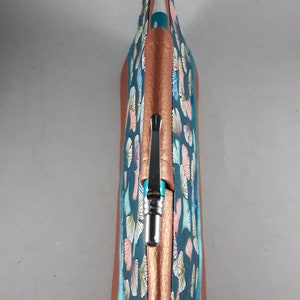 May include: A pen case with a teal and copper color scheme. The case features a pattern of stylized leaves in shades of pink, blue, and yellow. The pen case is made of a textured material and has a copper-colored zipper and trim.