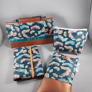 May include: A collection of teal and brown accessories, including a clutch, a zippered pouch, a notebook, and a phone case. Each item features a teal fabric with a floral pattern in pink, blue, and white, and a brown leather-like base.