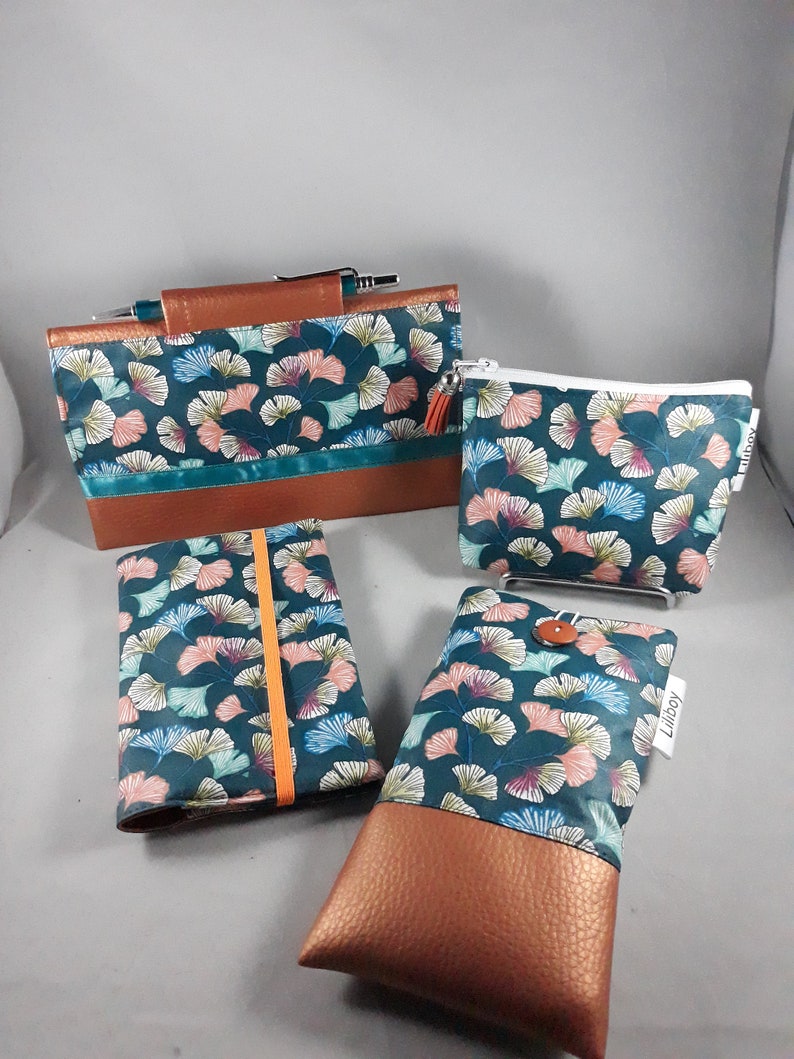 May include: A collection of teal and brown accessories, including a clutch, a zippered pouch, a notebook, and a phone case. Each item features a teal fabric with a floral pattern in pink, blue, and white, and a brown leather-like base.