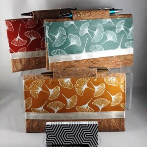 May include: Cork and fabric pen holders in red, teal, and mustard yellow, each featuring a white ginkgo leaf pattern. A silver band accents the fabric. A business card holder with the text "LILIBOY cr&eacute;ations" is in front.