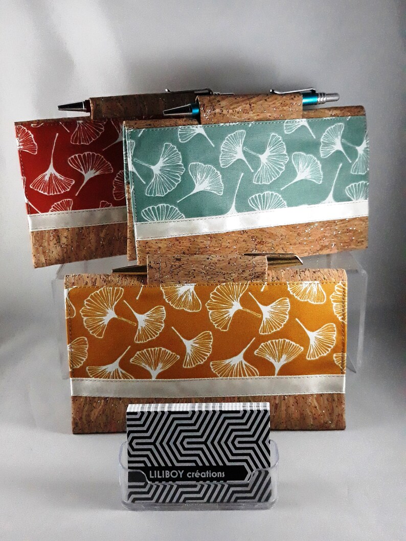 May include: Cork and fabric pen holders in red, teal, and mustard yellow, each featuring a white ginkgo leaf pattern. A silver band accents the fabric. A business card holder with the text "LILIBOY cr&eacute;ations" is in front.
