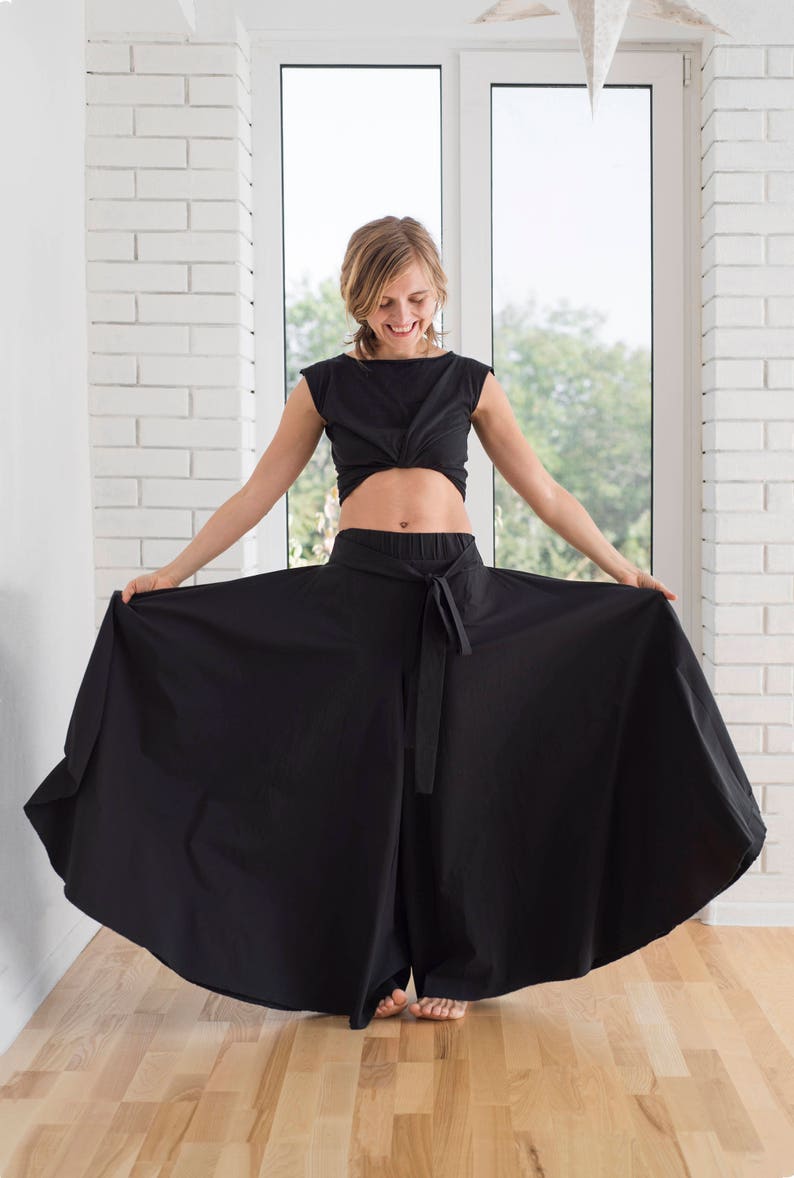 May include: A woman wearing a black crop top and wide-legged pants with a tie belt. The pants are flowing and billowing.