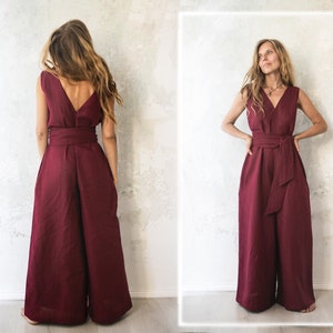May include: A burgundy linen jumpsuit with a V-neck and a wide leg. The jumpsuit has a tie belt at the waist.