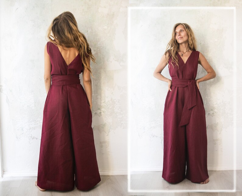 May include: A burgundy linen jumpsuit with a V-neck and a wide leg. The jumpsuit has a tie belt at the waist.